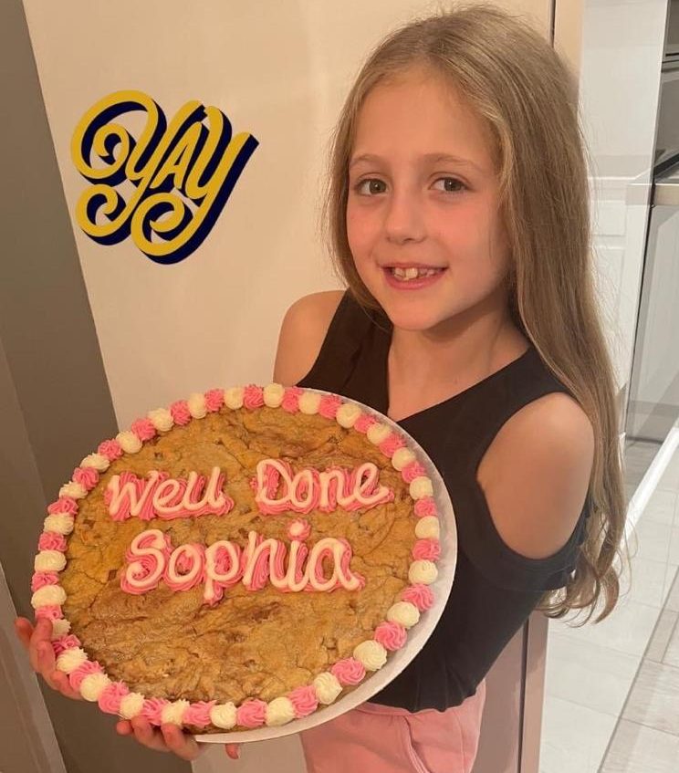 Sophia posing with a cake that reads "Well Done Sophia!"